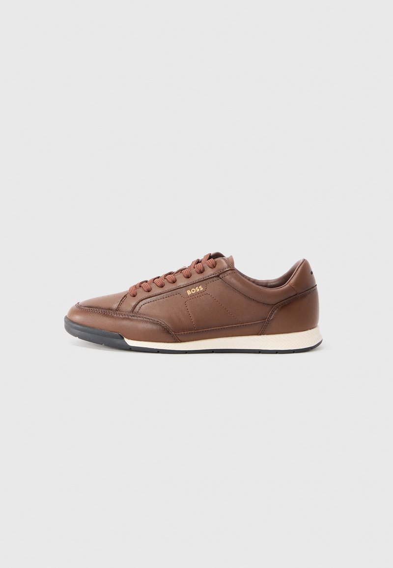 Baskets en cuir marron avec bout rond, fermeture à lacets, couture discrète et semelle blanche texturée. Minimalisme de la marque sur le côté.