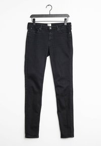 Svarta slim-fit jeans tillverkade av denim, med standard femfickorsdesign, knäppning och bälteshällor, hängande på en svart galge.