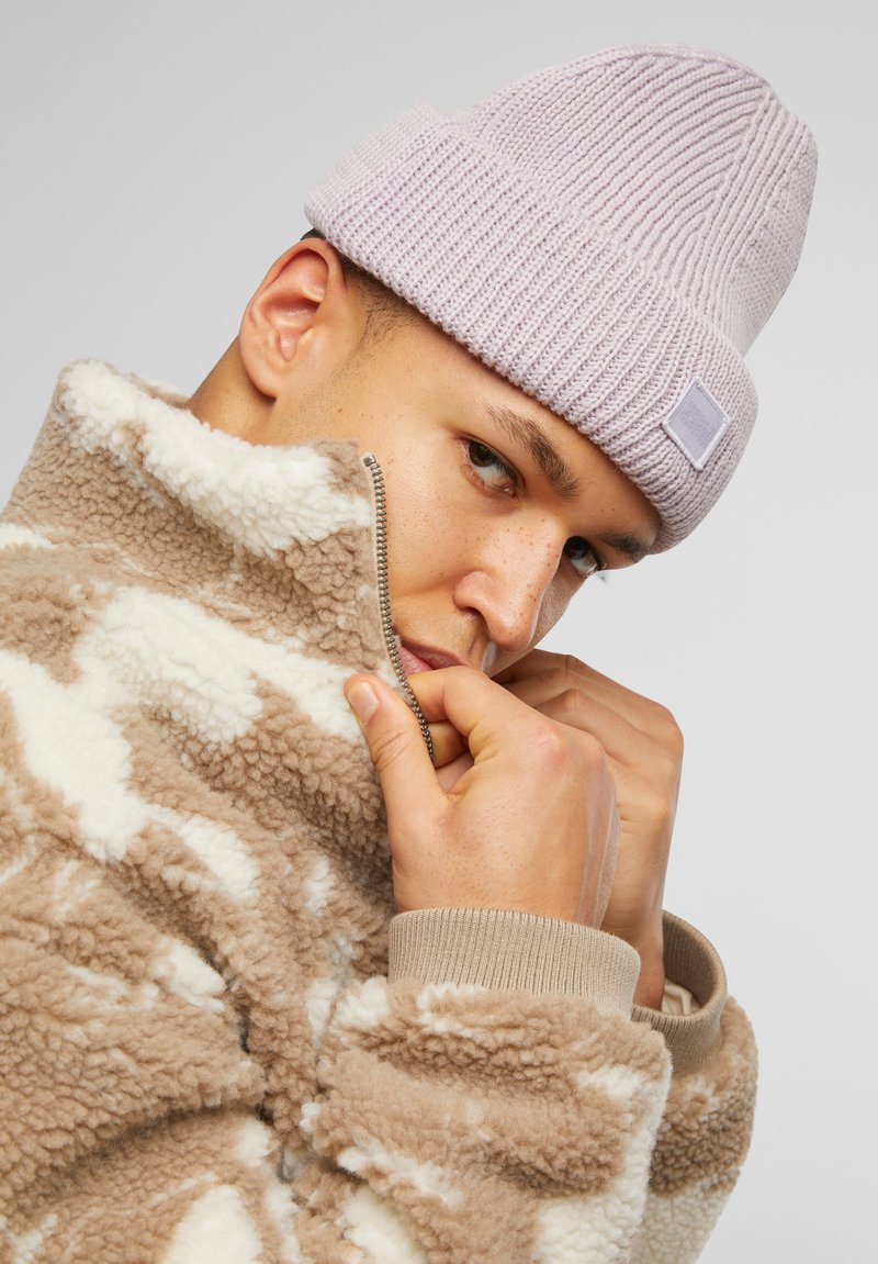 Light purple ribbed knit beanie and brown fleece jacket with white abstract patterns, featuring a zippered collar and textured fabric.