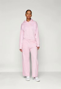 Pink tracksuit set made of soft fabric, featuring a zip-up hoodie and wide-leg pants. Includes elastic cuffs and a discreet logo detail.