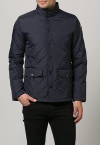 Marineblauer, gesteppter Mantel aus leichtem Material mit hohem Kragen, Knopfschluss und zwei vorderen Taschen mit Klappendetails.