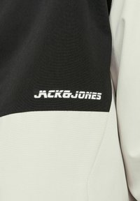 Giacca bianca e nera con un tessuto texturizzato, con un logo prominente "JACK & JONES" in bianco sulla parte nera.