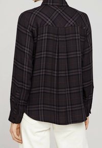 Svart flanellskjorta med grå och orange rutmönster, långa ärmar, knäppta manschetter och en ryggsömn för extra textur och passform.