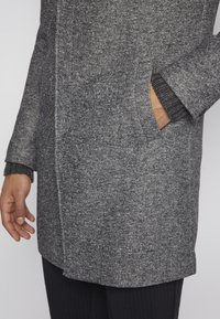 Grauer Mantel aus Wollmischung mit strukturierter Oberfläche, Seitentaschen und gerippten Bündchen. Das Design zeichnet sich durch einen geraden Schnitt und dezente Nahtdetails aus.