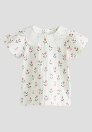 Vit skjorta med ett blommönster som har rosa blommor och gröna blad. Rynkade ärmar och en krage med spetskant. Randig textur.