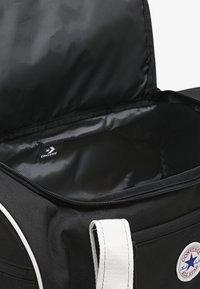 Mustast vastupidavast kangast duffelkott, millel on sile vooder. Disainis on valged detailid ja Converse'i logomärk. Tõmblukuga sulgur.