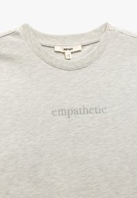 Camiseta de algodón gris claro con cuello redondo y la palabra "empático" en un sutil texto impreso en el pecho.