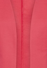 Tissu corail avec une texture lisse. Il présente une couture centrale et deux revers inclinés, créant un design structuré.