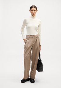Slimfittet elfenbensfarvet turtleneck top med flæset krave, parret med højtaljede beige brede bukser og sorte ankelstøvler, mens hun bærer en sort håndtaske.