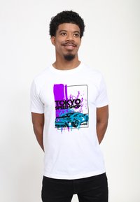 Bílý bavlněný tričko s grafickým designem modrého auta a fialových barevných skvrn, s textem "TOKYO SPEED SHOP" v tučném černém písmu.
