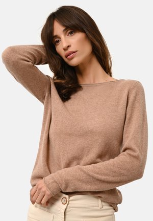 Hellbrauner Pullover aus weichem Stoff, mit langen Ärmeln und Rundhalsausschnitt. Kombiniert mit cremefarbenen Hosen, die eine lässige Passform zeigen.