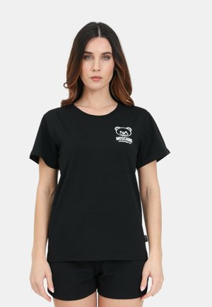 T-shirt nera in cotone con scollatura rotonda, maniche corte e logo della mascotte Moschino bianco stampato sul lato sinistro del petto. Abbinata a pantaloni corti neri.