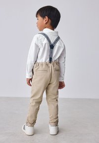 Beige elastic waistband pants with back pockets, paired with a white button-up shirt and navy-striped suspenders. White sneakers detail "BAKER."