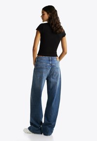 Czarna dopasowana bluzka z krótkim rękawem w połączeniu z jasnoniebieskimi spodniami typu wide-leg, z brązową skórzaną naszywką z tyłu i dwiema tylnymi kieszeniami.