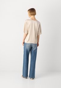 Beige kortermet topp laget av glatt stoff, parret med løse blå denimbukser med en liten falming, og uformelt fottøy.