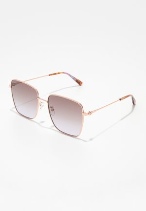 Occhiali da sole di forma quadrata con sottile montatura in metallo color oro rosa e lenti sfumate grigie, poggiati su una superficie bianca.