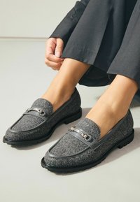Grå flade loafers med en sort gummisål, der har en sølvkæde accent foran og en rund tådesign.