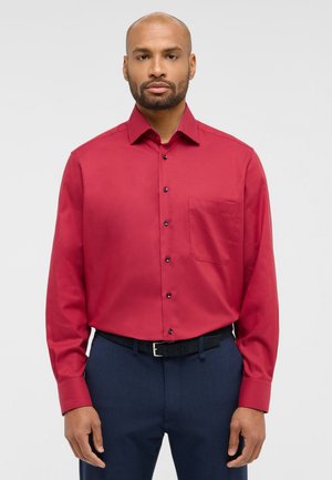 Rotes langärmliges Hemd mit Knopfleiste und Brusttasche. Mit Kragen und schwarzen Knöpfen, kombiniert mit dunkelblauen Hosen und einem schwarzen Gürtel.