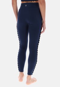 Námornícke legíny s vysokým pásom, ktoré majú hladkú textúru, priliehavý strih a vlnité akcenty po stranách. Mäkká, elastická tkanina.