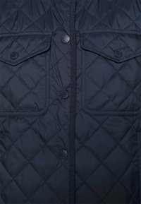 Gilet trapuntato blu navy con motivo a rombi, dotato di due tasche sul petto con bottone e apertura frontale chiusa da bottoni e cerniera.