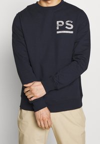 Sudadera azul marino de mezcla de algodón, con cuello redondo, mangas largas y un logo "PS" blanco con diseño en el pecho.