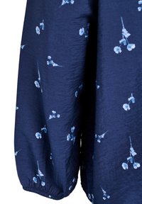 Mornarska tkanina s topom z majhnim svetlom modrim cvetličnim vzorcem. Ima elastične manšete in mehak, teksturiran površinski sloj. Poudarek na rokavih in cvetličnih detajlih.