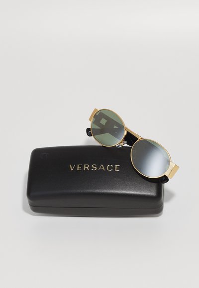 Okrogle sončne naočnike z zlatimi okvirji in zelenimi lečami, prikazane na črni etui s pozlačenim napisom "VERSACE".