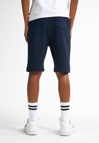 Marineblauwe katoenen shorts met een rechte snit, voorzien van een achterzak en een rafelzoom. Gecombineerd met witte sokken met zwarte strepen en witte schoenen.