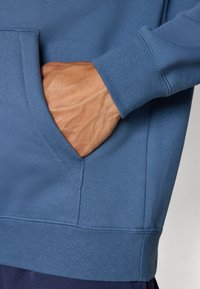 Blaues Sweatshirt mit einer Fronttasche, gerippten Bündchen und Saum. Der Stoff hat eine glatte Textur und einen lässigen Schnitt.