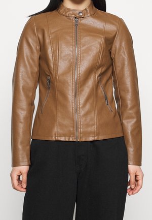 Vrouw draagt een nauwsluitend bruin leren jack met een voorrits, ritssluitingen aan de zijkanten en een drukknoopkraag, gecombineerd met losse zwarte broek.