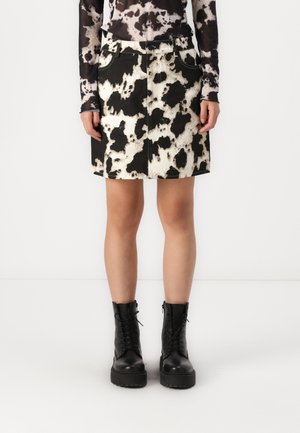 Jupe en denim imprimée vache noir et blanc avec deux poches avant, une fermeture éclair et une silhouette ajustée. Associée à des bottines de combat lacées noires.