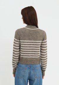 Brun og hvid stribet sweater med høj hals og ribbede manchetter, lavet af blødt stof, kombineret med blå højtaljede jeans.