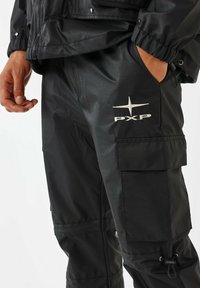 Zwarte cargobroek met een textuurafwerking, zijzakken, verstelbare enkelsluitingen en een wit "PXP" logo op de dij.