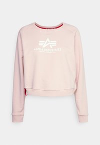 Růžová krátká mikina s kulatým výstřihem, s bílým logem "Alpha Industries" a červenými detaily po stranách. Měkká textura látky.