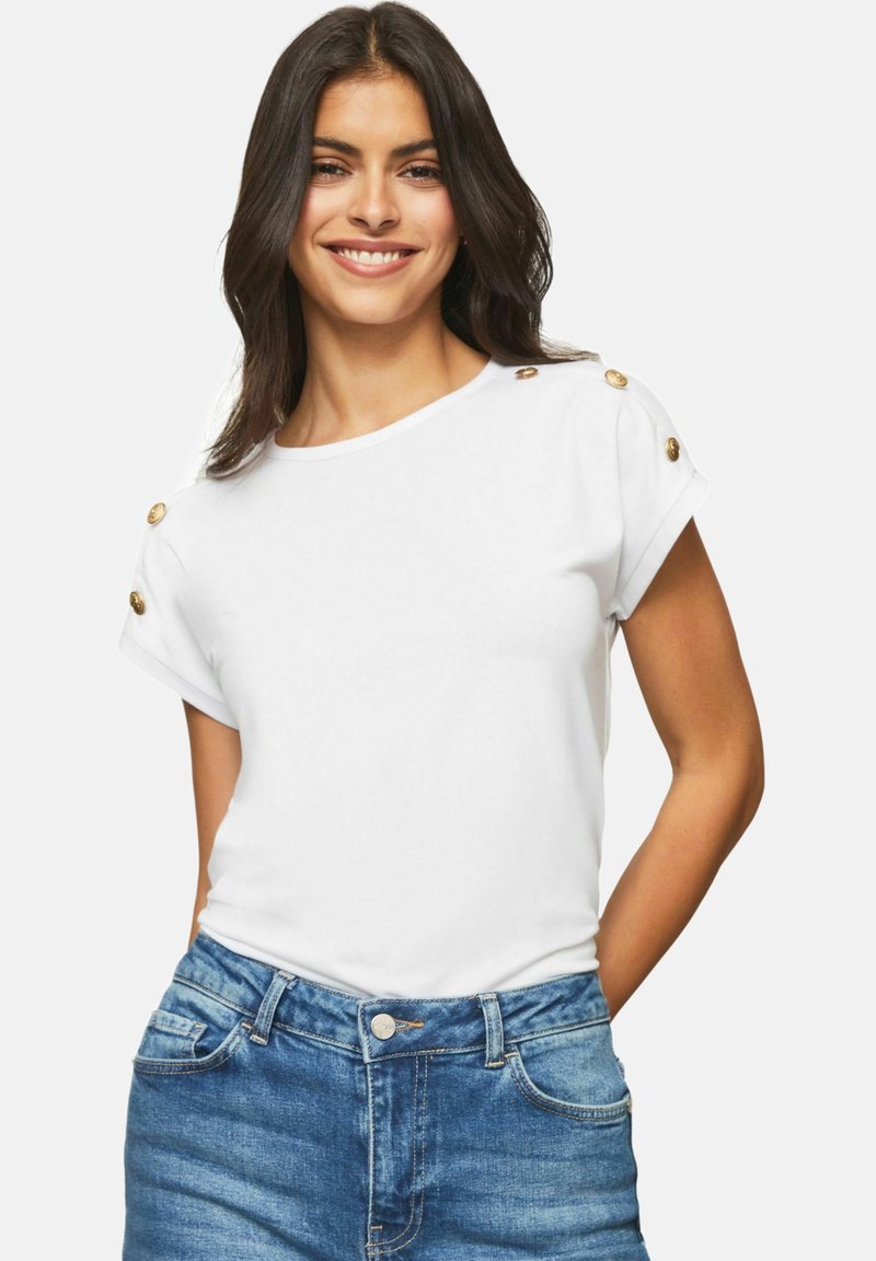 Hvid kortærmet T-shirt lavet af bomuld, med guld knapdetaljer på skuldrene og en afslappet pasform, parret med blå denimshorts.