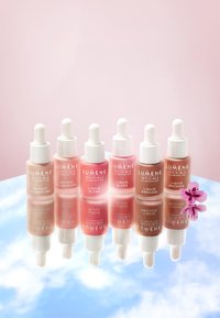 Siete botellas de vidrio con gotero y tapas blancas. Los colores incluyen rosa claro, rubor y bronce. Cuentan con etiquetas de texto con nombres de productos.