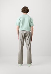 Gaiši zaļa kokvilnas T-kreklis ar īsām piedurknēm, kombinēts ar pelēkiem, nedaudz vaļīgiem biksēm. Ikdienas apavi ar zaļiem akcentiem.