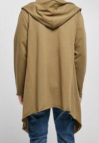 Sudadera con capucha marrón, con un dobladillo trasero largo y detalles de borde sin acabar. Fabricada en una tela suave, presenta un corte relajado y mangas largas.