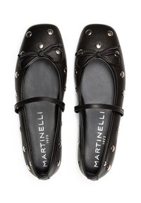 Zapatos planos de cuero negro con punta cuadrada, adornos metálicos decorativos y un lazo en la parte delantera. Incluyen una correa delgada para el tobillo.