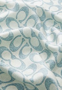 Tkanina z jasnoniebieskim i białym wzorem wzajemnie przenikających się kształtów. Materiał ma miękkie, teksturowane wykończenie z subtelnymi odcieniami w designie.