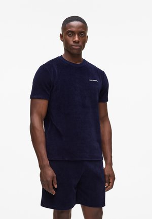Marineblå frotté T-shirt med korte ærmer og rund hals, med et lille hvidt logo på brystet. Blød tekstur, afslappet pasform.