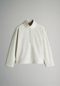 Biely fleecový pulóver s vysokým golierom a krátkym zipsom. Má dlhé rukávy a mierne voľný strih. Mäkkučká textúra.