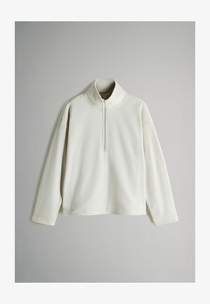 Biely fleecový pulóver s vysokým golierom a krátkym zipsom. Má dlhé rukávy a mierne voľný strih. Mäkkučká textúra.