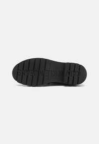 Semelle de chaussure noire avec des rainures profondes et "CALVIN KLEIN JEANS" embossé sur le dessous pour le détail de la marque et de la traction.