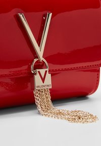 Borsa a tracolla in pelle rossa brillante con un emblema dorato a forma di "V", dettagli a catena e un lucchetto rettangolare con la scritta "VALENTINO" incisa.