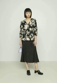 Blusa preta com estampado floral e mangas três quartos, combinada com uma saia preta até ao joelho. Os acessórios incluem uma pequena mala lilás claro e tamancos pretos.