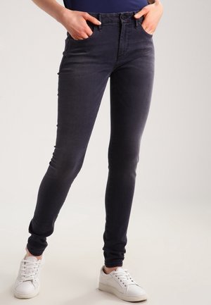 Vaqueros ajustados en denim gris oscuro con una textura suave, que presentan una cintura de altura media y bolsillos frontales, combinados con zapatillas blancas.