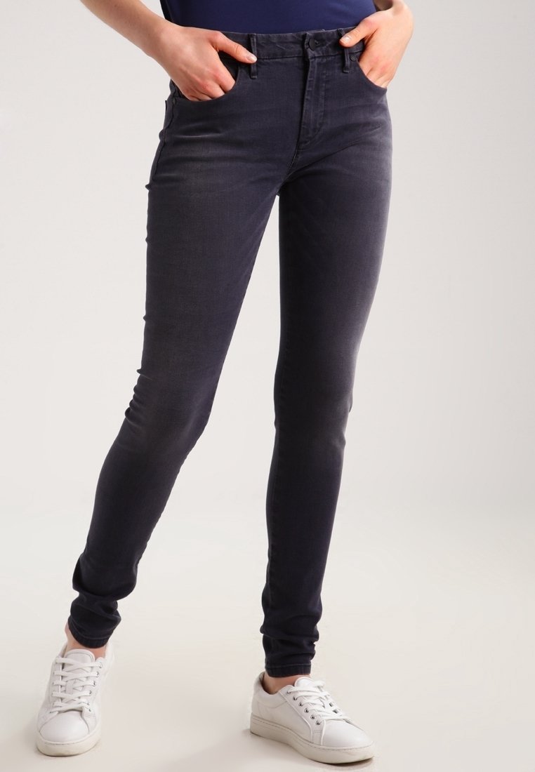 Vaqueros ajustados en denim gris oscuro con una textura suave, que presentan una cintura de altura media y bolsillos frontales, combinados con zapatillas blancas.