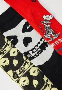 Three pairs of socks: a black and white skull design, a yellow skull pattern, and a red sock featuring a skeleton dog with graphic text.