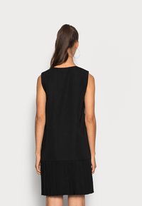 Abito nero senza maniche con una parte superiore liscia e una gonna plissettata. Nessun hardware o motivo visibile. Colore uniforme in tutto.